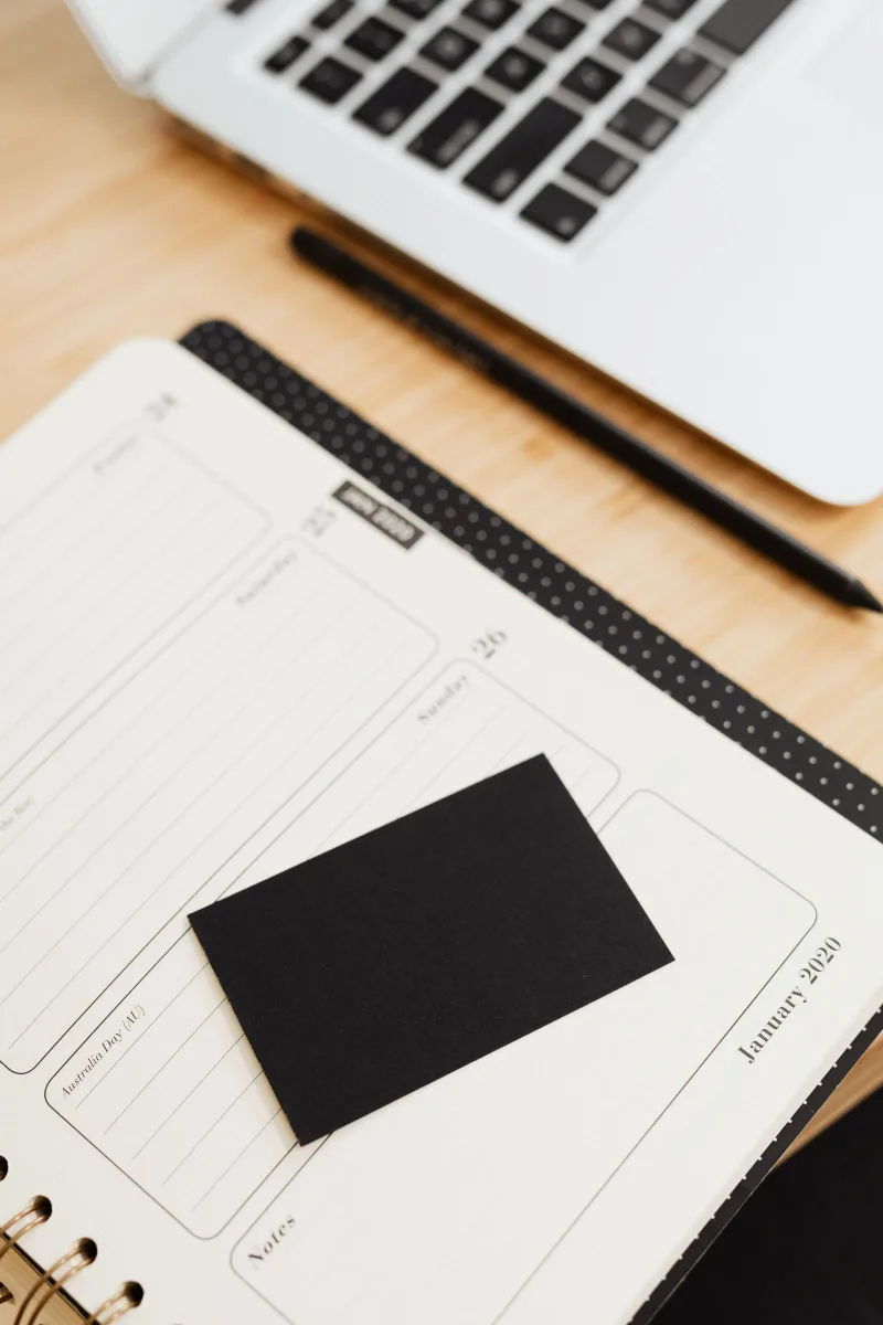 An open paper planner beside a laptop and pen.