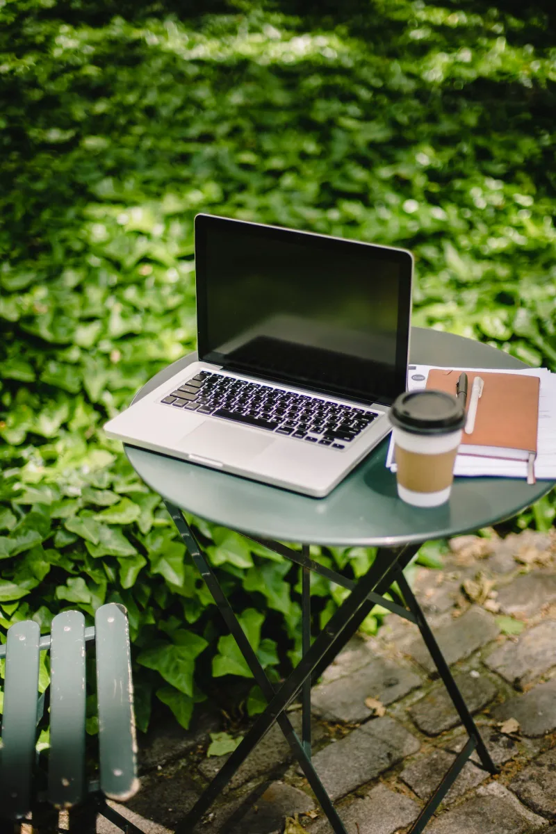 Laptop, notebook and takeaway coffee on a table outside.