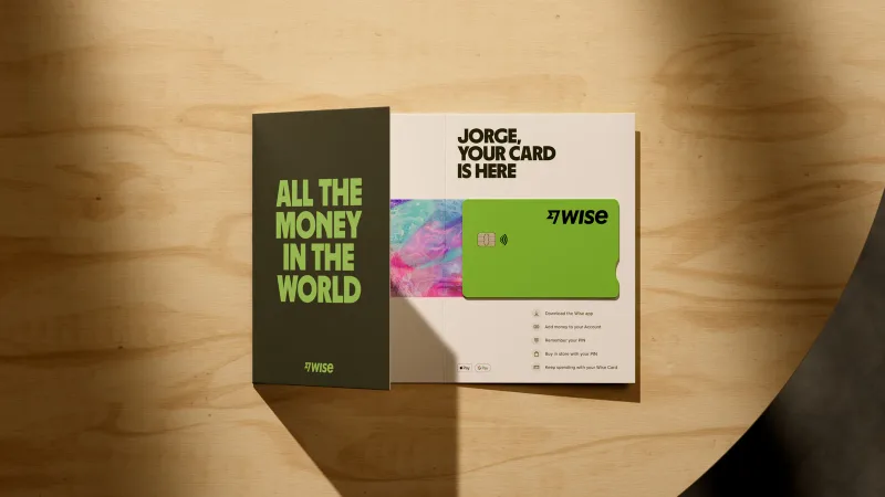 A green Wise debit card in its welcome packaging on a wooden table.